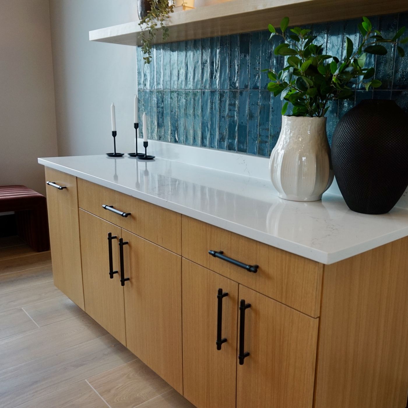 Finished cabinet detail with wood drawers, black pulls, quartz counter, and blue tile backsplash